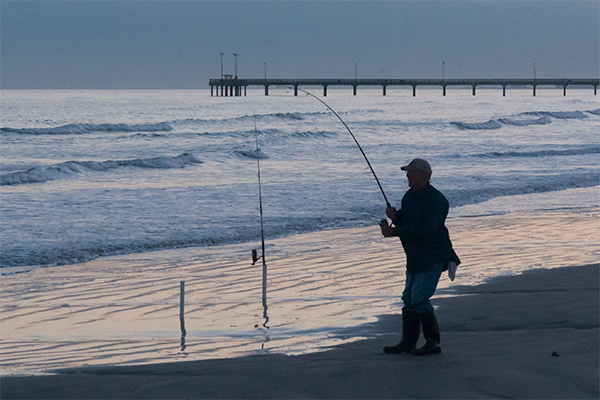 Man fishing on the beach at sunset